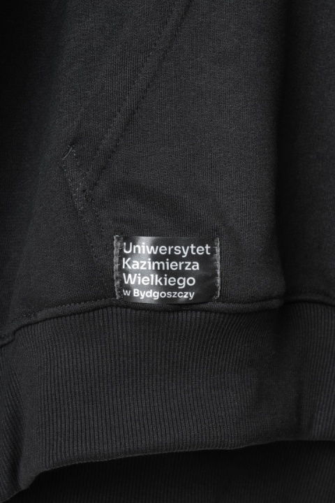 Naszywka z nazwą Uniwersytetu Kazimierza Wielkiego w Bydgoszczy na czarnej bluzie.