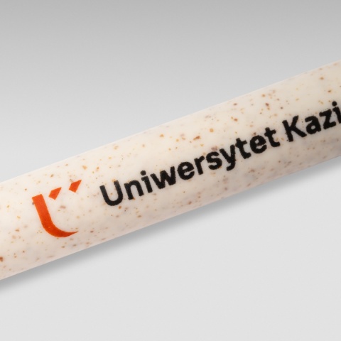 Zbliżenie na logo Uniwersytetu Kazimierza Wielkiego umieszczone na beżowym długopisie ze słomy pszenicznej.
