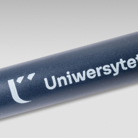 Zbliżenie na logo Uniwersytetu Kazimierza Wielkiego umieszczone na granatowym długopisie ze słomy pszenicznej.
