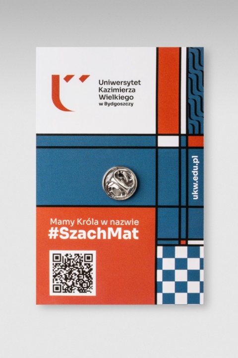 Tylna strona pinu z metalowym zapięciem oraz karta UKW z hasłem „Mamy Króla w nazwie #SzachMat”.