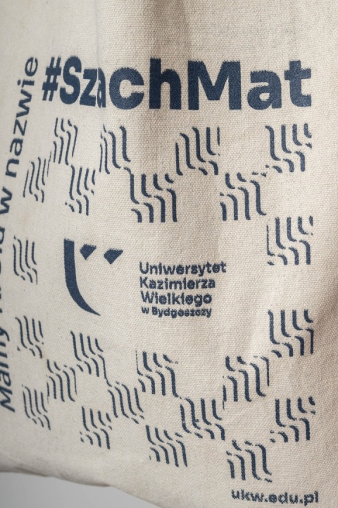 Zbliżenie na granatowy nadruk „#SzachMat”, logo oraz nazwę Uniwersytetu Kazimierza Wielkiego na bawełnianej torbie.