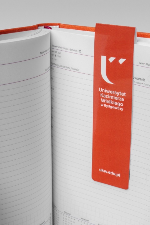 Pomarańczowa zakładka magnetyczna z logo UKW umieszczona na stronie otwartego kalendarza.